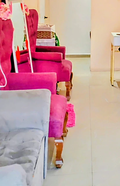 Fila de sillones capitoné fucsia para pedicure con patas de madera, junto a un sillón gris, en el pasillo del salón