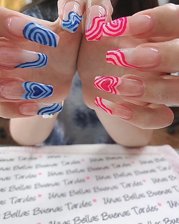 Dos manos con uñas largas de corazones concéntricos pintados a mano: azul rey en una mano y fucsia en la otra, sobre el mantel del salón