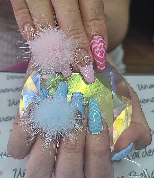 Uñas largas en rosa y azul cielo con pompones de pelusa, corazones concéntricos y cristalitos, sobre un cristal iridiscente